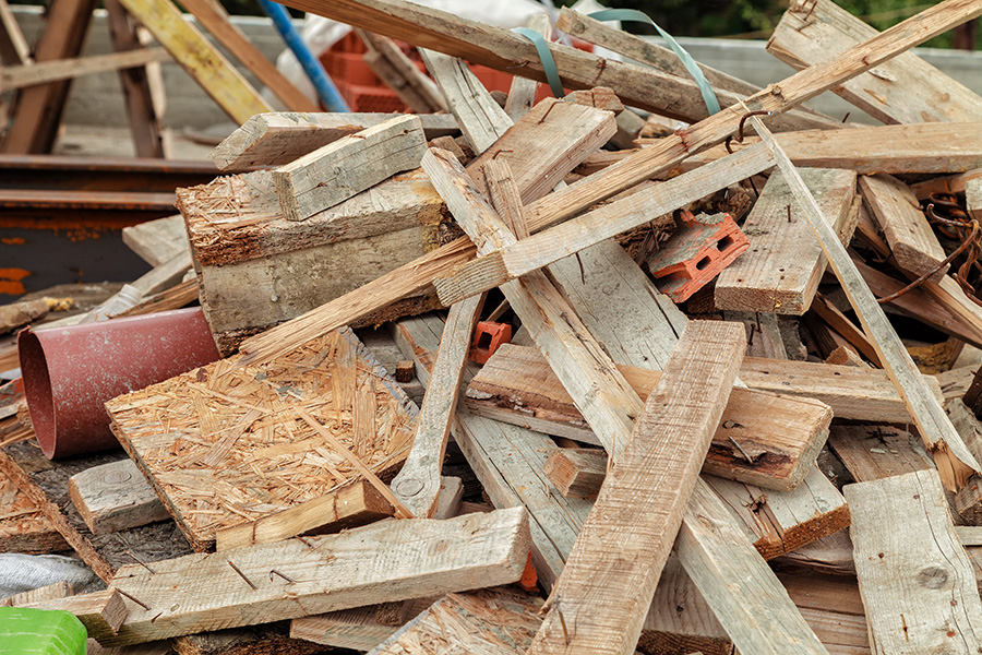A pile of assorted wooden planks and construction debris, including pieces of wood, nails, and a few bricks, scattered outdoors at what appears to be a construction or demolition site.