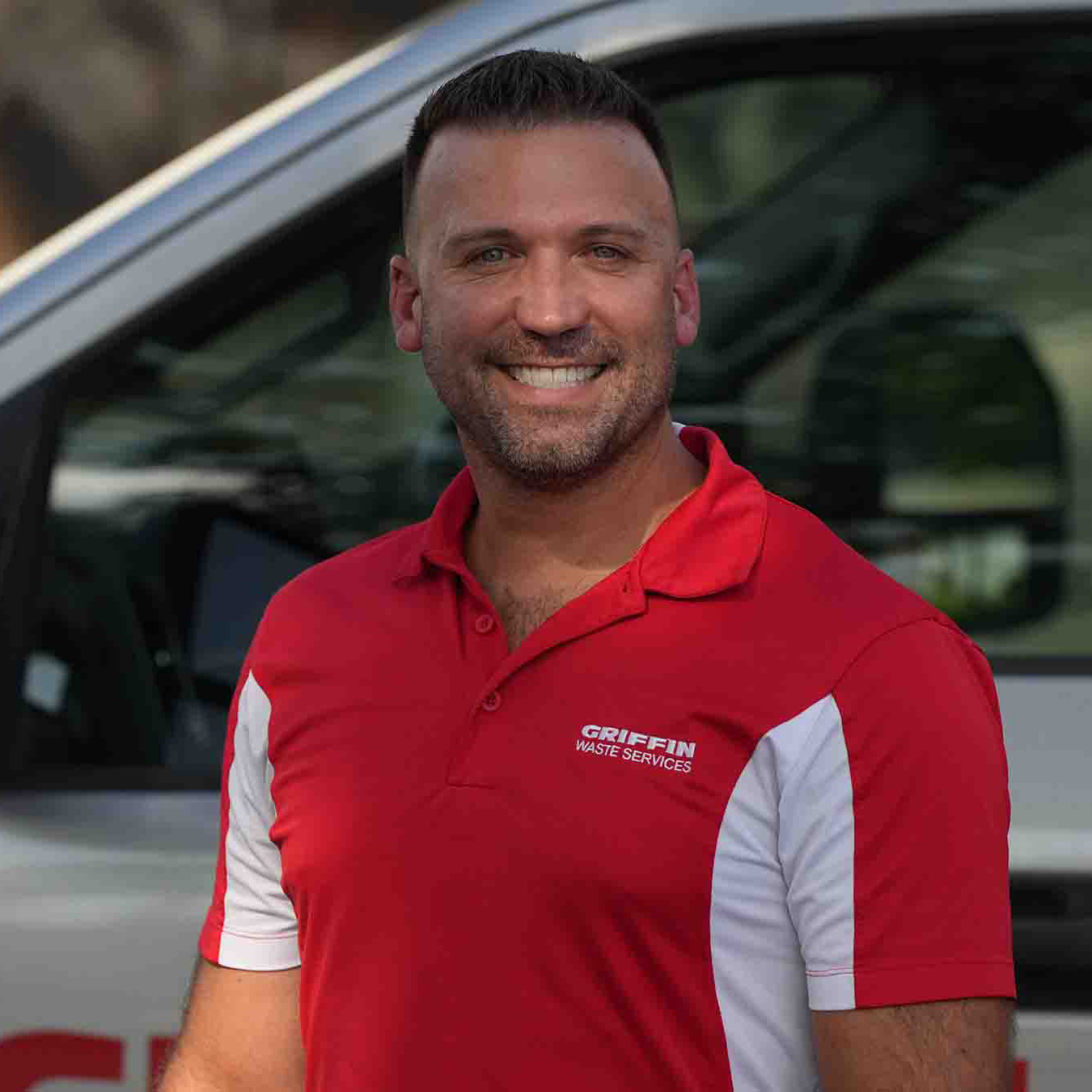 Ryan1 A smiling man wearing a red and white Griffin Waste Services polo shirt stands in front of a vehicle with a partial logo visible in the background.